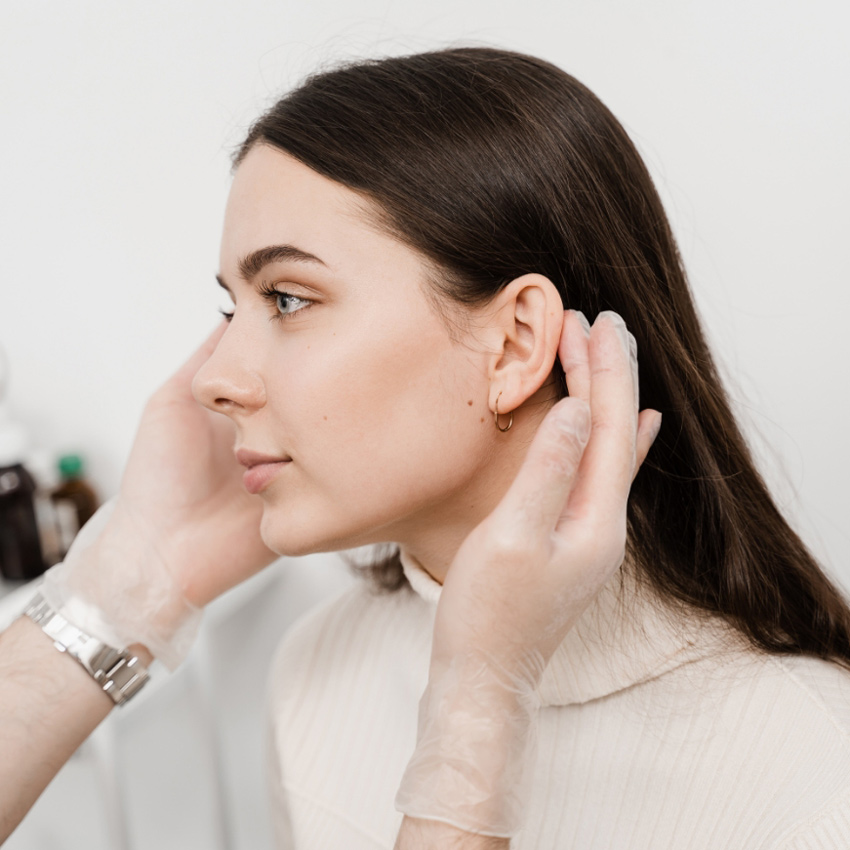 A woman’s profile as a gloved practitioner gently examines her ear.