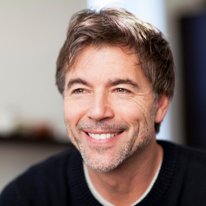A smiling man looks slightly off-camera with soft natural lighting.