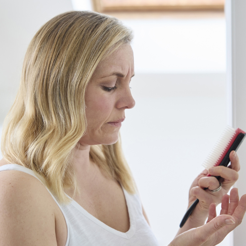 A woman looks down at hair in her hand while holding a brush.