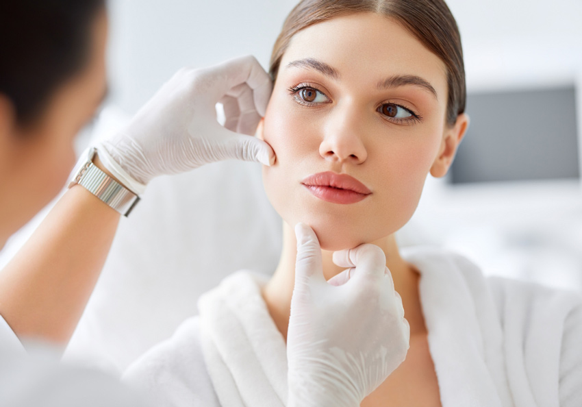 A clinician wearing gloves evaluates a woman’s cheek and jawline.