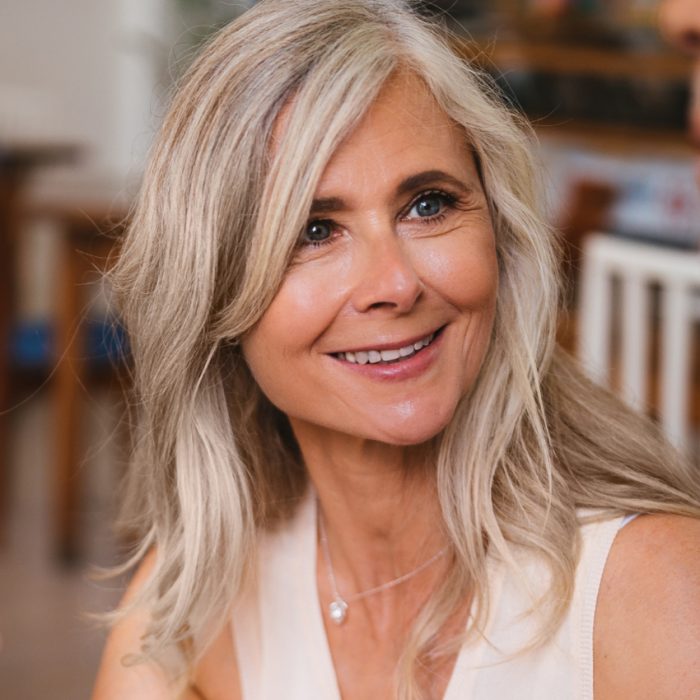 A woman with long silver hair smiles while looking slightly to the side.
