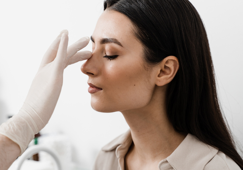 A gloved clinician gently presses the tip of a person’s nose during an examination.
